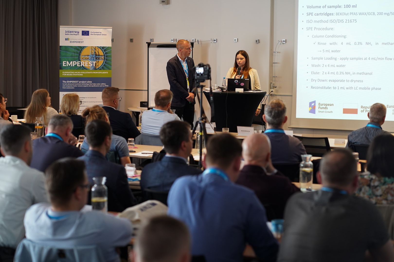 Prof. Rafał Rakoczy i dr hab. inż. Paula Ossowicz-Rupniewska, prof. ZUT, podczas prezentacji na seminarium EMPEREST w Szczecinie, przed publicznością składającą się z europejskich specjalistów branży wodno-ściekowej; widoczny ekran z procedurą analityczną oraz baner projektu EMPEREST