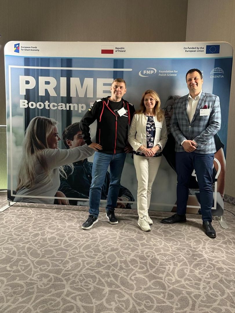 Trzy osoby stojące przed banerem PRIME Bootcamp z logotypami Funduszy Europejskich, Rzeczypospolitej Polskiej, Fundacji na rzecz Nauki Polskiej oraz Unii Europejskiej